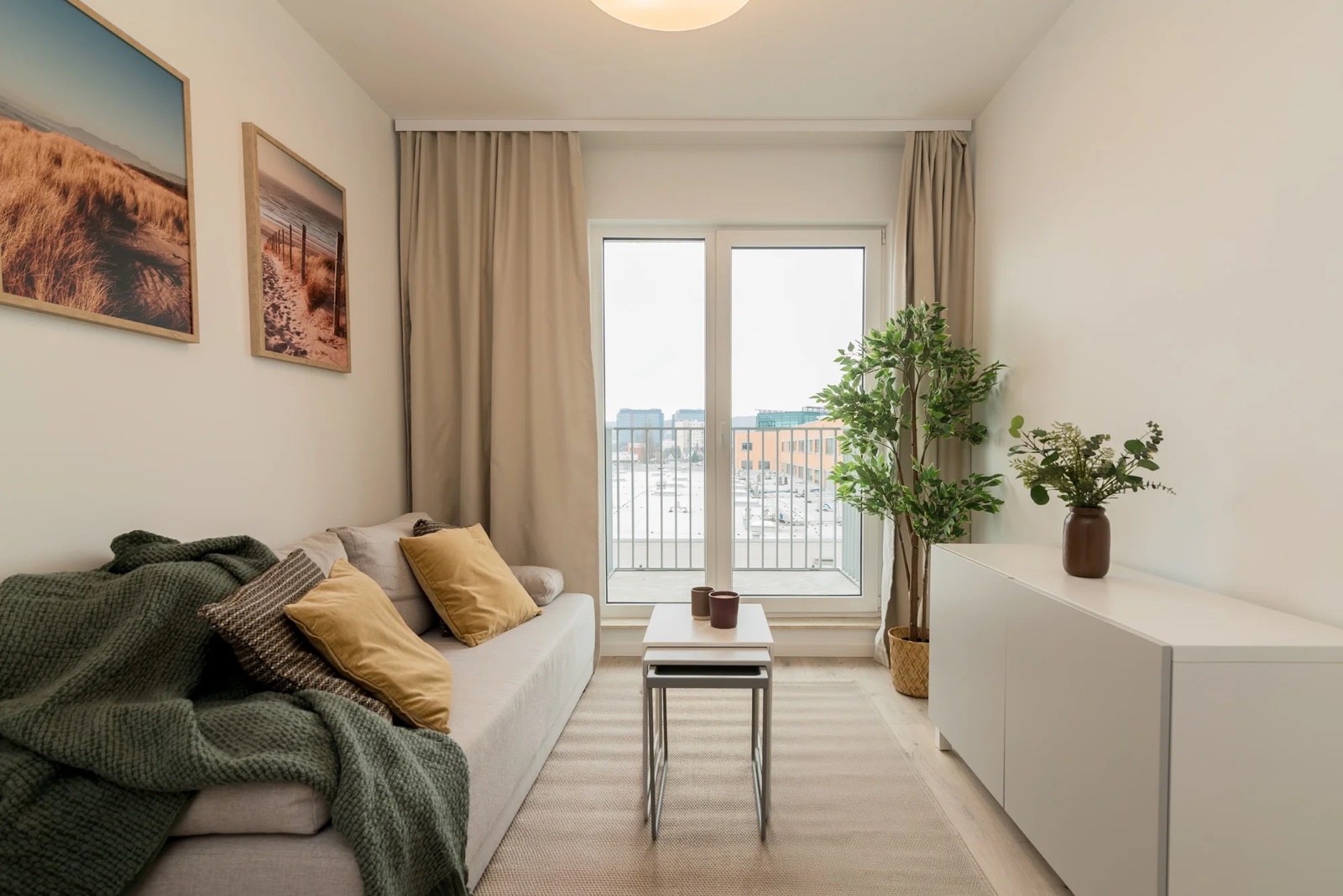 Salon z jasną sofą, żółtymi poduszkami i wyjściem na balkon.